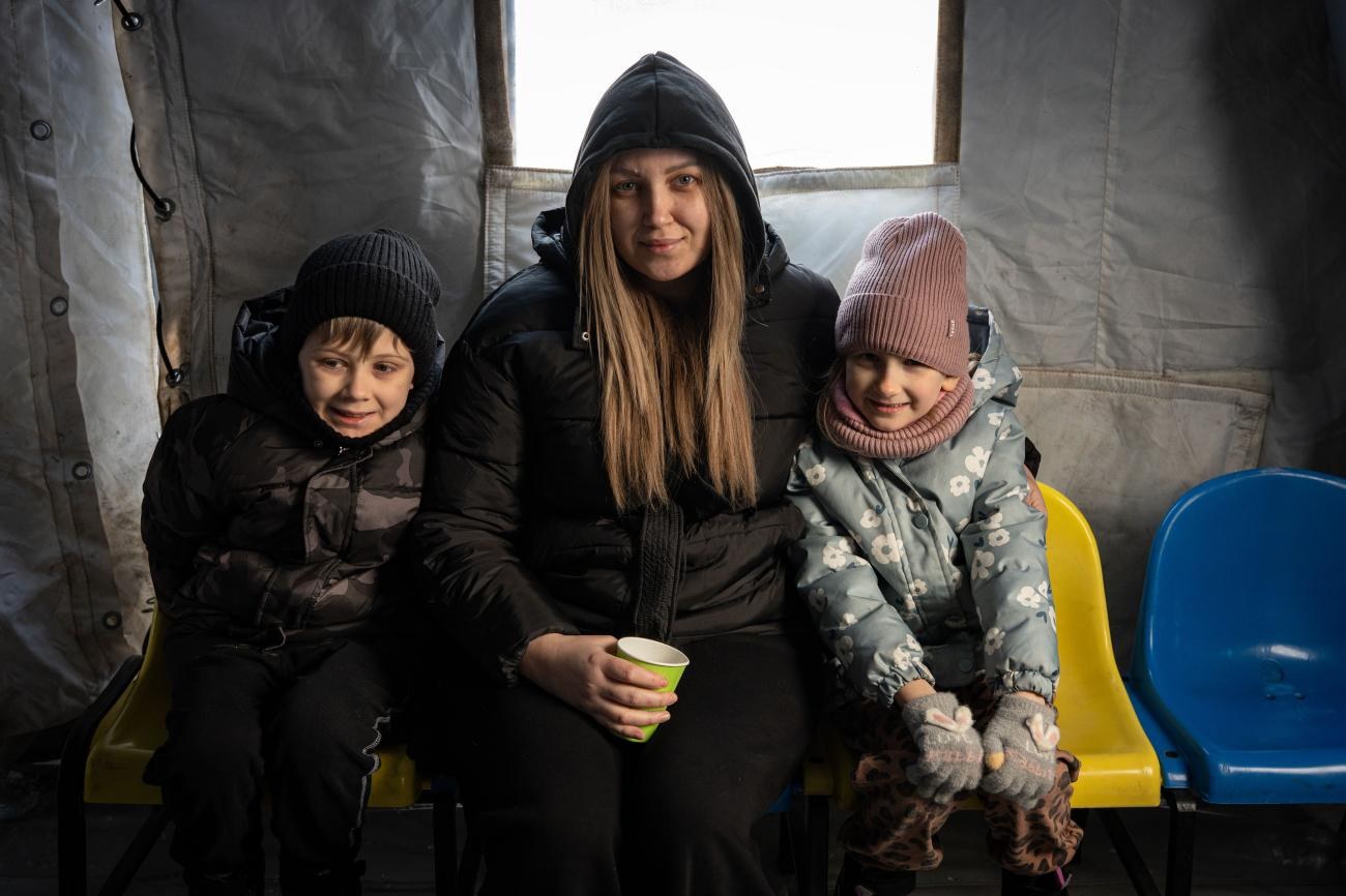 A woman and her two children warming up at a heating point in a tent